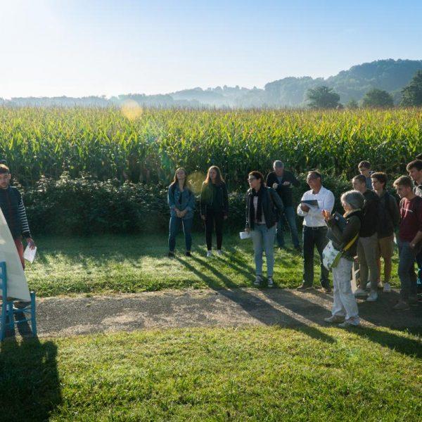 Un étudiant et une étudiante montrent des croquis d'aménagement en bordure du terrain du Foyer, devant les champs de maïs voisins et les collines environnantes.