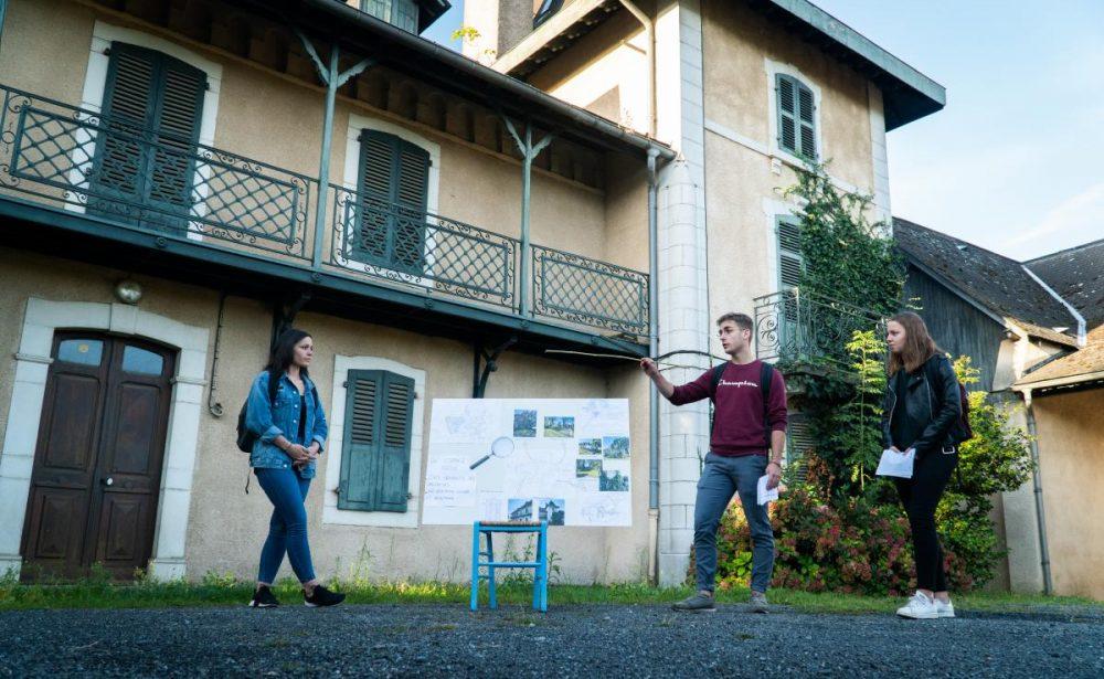 Deux étudiantes et un étudiant présentent un projet d'aménagement dans la cour de l'ancienne batisse.