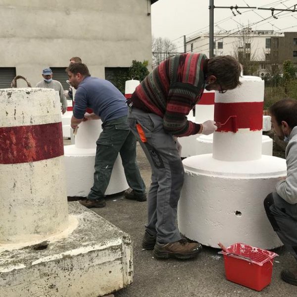 Des ouvriers sont en train de peindre des plots de sécurité.