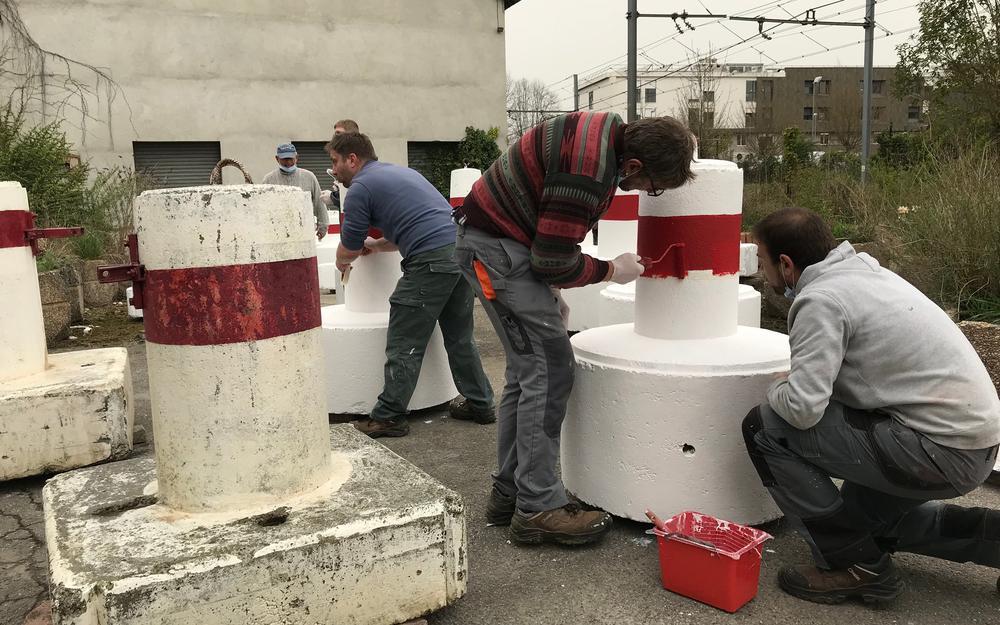 Des ouvriers sont en train de peindre des plots de sécurité.
