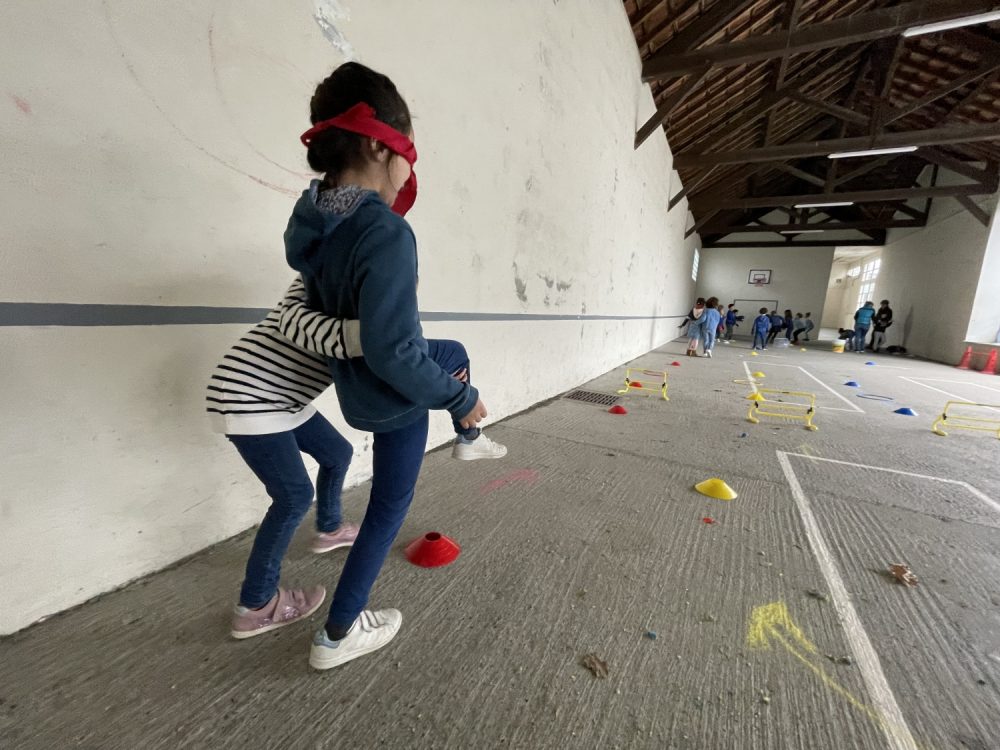 Une enfant guide une autre enfant sur un parcours psychomoteur.