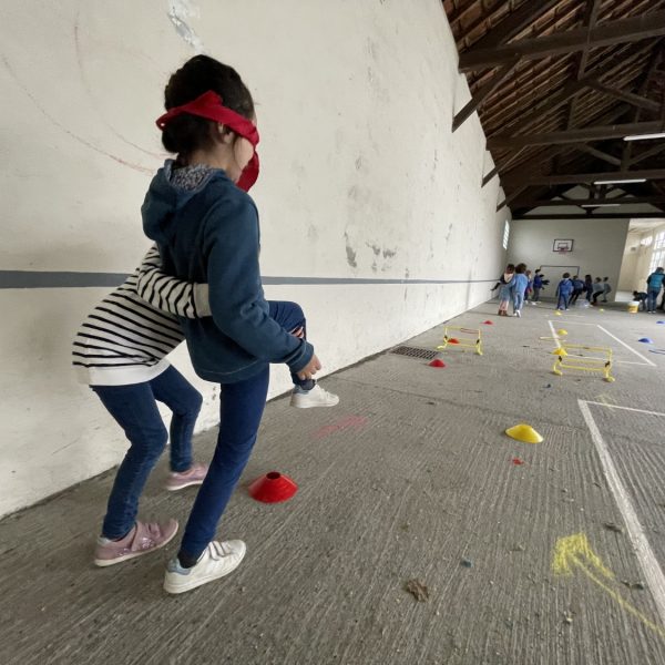 Une enfant guide une autre enfant sur un parcours psychomoteur.